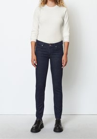 Tmavě modré džínové skinny džíny s středním pasem, s pěti kapsami a zapínáním na knoflík, kombinované s krémovým pleteným topem s dlouhým rukávem.