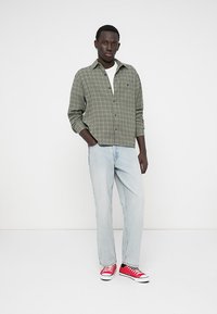Grønternet skjorte med knaplukning, parret med lyseblå jeans og røde sneakers. Enkelt, afslappet outfit med kontrastfarver.