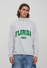 Felpa grigia con zip e la scritta "FLORIDA" e "EAST 1990" stampata in verde. Presenta un collo alto e polsini a costine, realizzata in un tessuto morbido.
