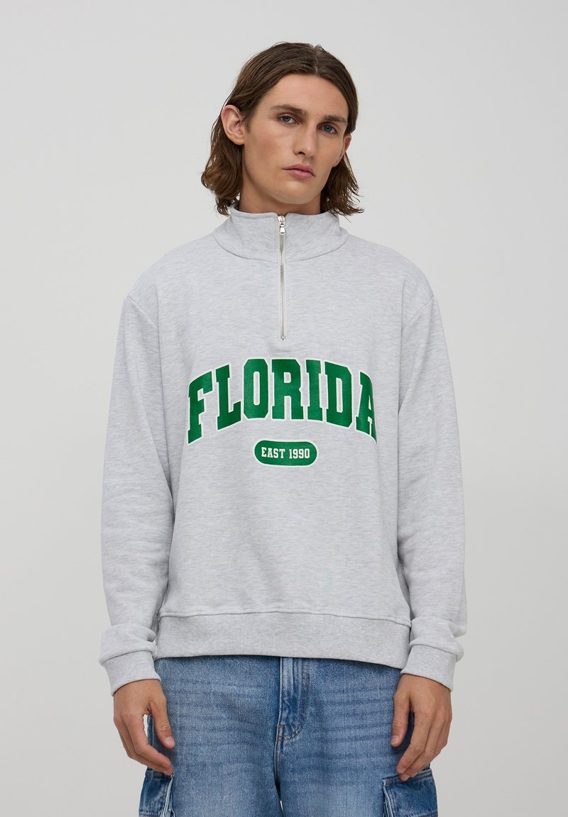 Felpa grigia con zip e la scritta "FLORIDA" e "EAST 1990" stampata in verde. Presenta un collo alto e polsini a costine, realizzata in un tessuto morbido.
