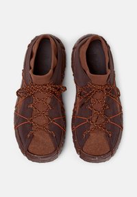 Bruna sportskor med textilöverdrag och orange snören, sedda från ovan, som visar deras robusta design och stötdämpande struktur.