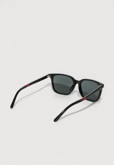 Ochelari de soare negri cu rame pătrate, lentile gri și un finisaj lucios. Acest model are accente cu dungi roșii pe brate. Designul general este elegant.