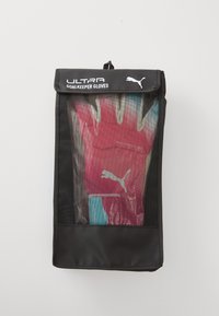 Fekete hálós tasak, amelyen Ultra Kapus Kesztyű felirat található, benne egy pár piros és kék Puma kapus kesztyű.