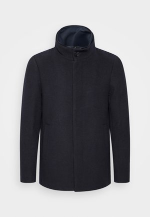 Mörk marinblå kappa med hög krage, minimala sömmar, knäppning framtill och sidofickor. Tyget verkar slätt med en lätt textur.