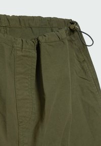 Close-up van olijfgroene broeken met een elastische tailleband en verstelbaar trekkoord voor een veilige pasvorm.