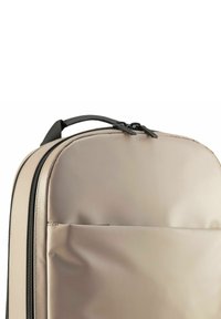 Beige rugzak met een gladde textuur, voorzien van twee zwarte ritsen en een handvat aan de bovenkant. Inclusief een voorvak en een gebogen ontwerp.