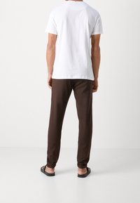 Camiseta blanca de algodón, pantalones marrones de algodón, corte relajado, textura suave, cintura ajustable, usados con sandalias negras, vistos desde atrás.