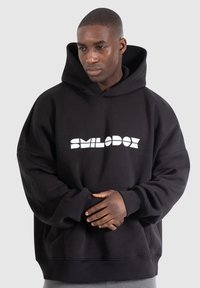 Black hoodie with a large white graphic logo, featuring a front pocket and ribbed cuffs at the sleeves and hem. Soft fabric texture.