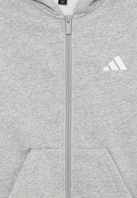 Gray zip-up hoodie made of cotton blend fleece. Features a front zipper, two lower pockets, and a white Adidas logo on the left chest.