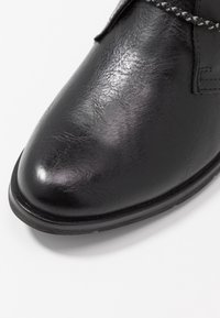 Bottine en cuir noir avec une finition lisse, bout rond, détails de couture et semelle texturée. Les lacets présentent un motif contrasté.