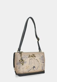 Bolso de mano con un cuerpo en beige claro, ilustraciones impresas, acentos negros y una correa gris. Presenta un charm en forma de corazón y texto decorativo.