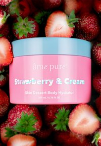 Rosa och blå burk märkt "Jordgubbs- och gräddhuddessert kroppshydrator", omgiven av färska jordgubbar, 200 mL.