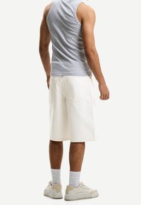 Šedý tílko a bílé džíny šortky, které mají volný střih a do délky ke kolenům. Boty jsou v neutrální barvě s bílými ponožkami.