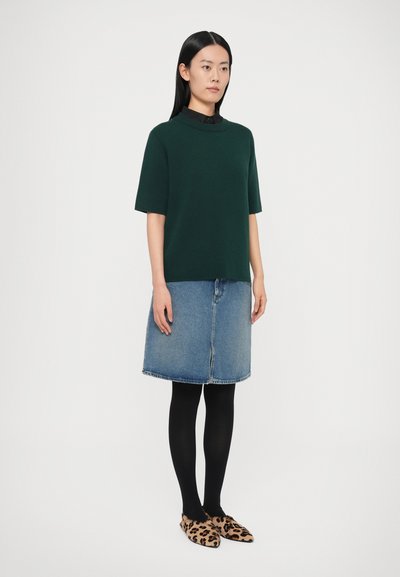 Zaļš īsroku trikotāžas tops kopā ar džinsa svārkiem. Melnas zeķubikses un dzīvnieku raksta leopardu raksta dzīvokļi noslēdz izskatu. Vienkāršs un ikdienišķs dizains.