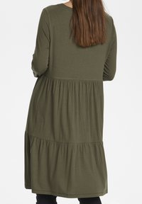 Oliwkowa sukienka z długim rękawem i warstwowym krojem, z dopasowanym gorsetem i luźną, zwiewną dolną częścią. Gładka faktura, okrągły dekolt.