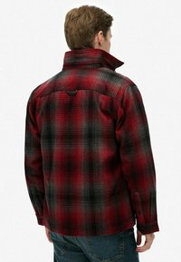 Rød og sort plaid flannel skjorte med høj krave, knapmanchetter og et struktureret stof. Har en central rygsøm og logoetiket.