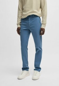 Light blue trousers with a slim fit, made of smooth fabric. Features side pockets and a subtle sheen, paired with white sneakers.