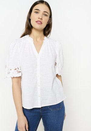 Weiße Bluse mit kurzen Puffärmeln und Spitzenrand. Mit V-Ausschnitt und Knopfleiste. Hergestellt aus einem leichten, strukturierten Stoff.