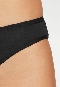 Perizoma in cotone nero con una cintura liscia e design a copertura minima. La texture è morbida e a coste.