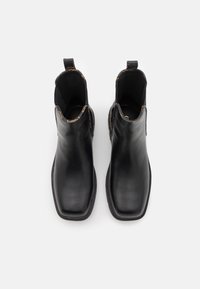 Bottines en cuir noir avec une finition lisse, bout carré, panneaux latéraux élastiques et languettes de traction. L'intérieur présente une doublure à motif subtil.