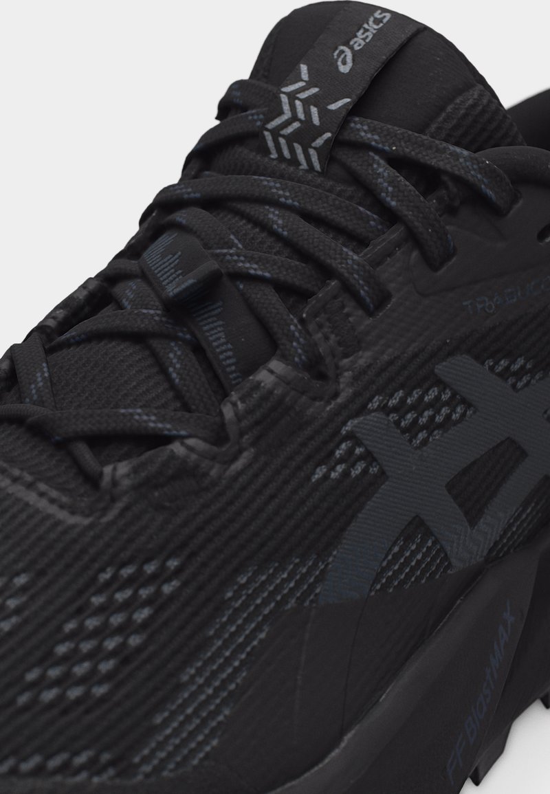 Gros plan sur une chaussure de course noire Asics avec un tissu texturé détaillé, des lacets, ainsi qu'une languette et des marquages latéraux de marque.
