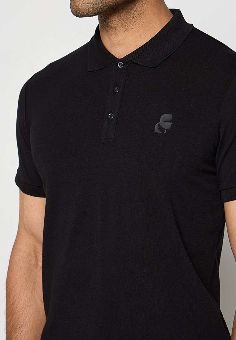 Polo noir en tissu texturé, avec une patte de boutonnage à trois boutons et un logo monochrome subtil sur la poitrine. Manches courtes.