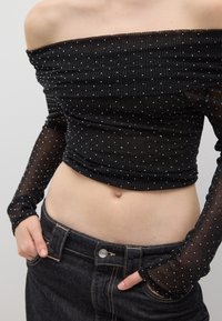 Top nero scollato con maniche lunghe trasparenti, caratterizzato da un design testurizzato e punti argentati, abbinato a jeans in denim scuri a vita alta.