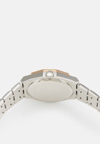 Montre octogonale en argent avec un accent doré sur le côté, bracelet en métal et fond de boîte gravé. Texture lisse avec une finition polie.