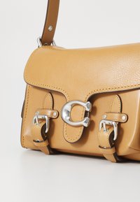 Tan leather handbag with a structured design, silver hardware, and dual buckle accents. Features a smooth texture and contrasting stitching.