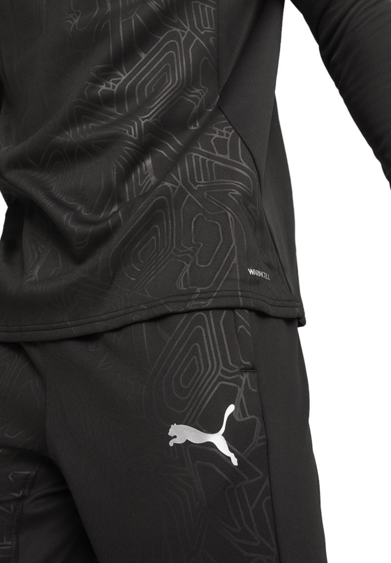 Schwarze Sportbekleidung mit strukturiertem Muster, langen Ärmeln und silbernem Puma-Logo. Hergestellt aus feuchtigkeitsableitendem Material.