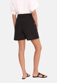 Czarne szorty o strukturze z wysokim stanem i wzorem w romby, zestawione z brązowymi płaskimi sandałami z detalem w postaci klamry.