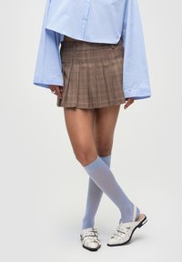 Gonna mini a pieghe a quadretti marroni, camicia azzurra a maniche lunghe, calze fino al ginocchio azzurre e sandali bianchi con accenti argentati.