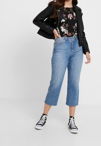 Veste en cuir synthétique noire, haut noir à fleurs, jean court taille haute bleu avec ourlet effiloché, accompagné de baskets noires et blanches.