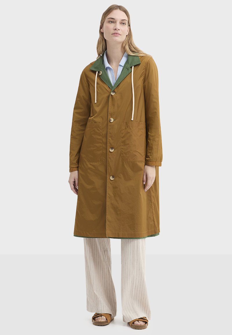 Imperméable marron longueur genoux avec col vert, boutons en bois, capuche à cordon et deux grandes poches avant. Texture lisse, matériau léger.