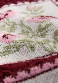 Strickstoff mit Blumenmustern in Pink- und Grüntönen, mit strukturierter Oberfläche und einem dunkelroten Rand entlang der Kante.