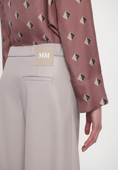 Ljusrosa byxor med elastisk midjeband och sidoficka, parat med en brun mönstrad långärmad blus med triangulära motiv.