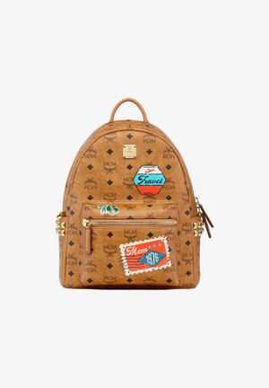 Brauner Leder-Rucksack mit bedruckten Logos, reise-themed Patches, einer Front-Reißverschlusstasche und goldenen Pyramidennieten an den seitlichen Akzenten.