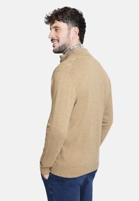 Suéter de punto marrón claro con cuello alto, corte recto y puños acanalados, combinado con una camisa de cuadros, mostrado desde la parte de atrás.