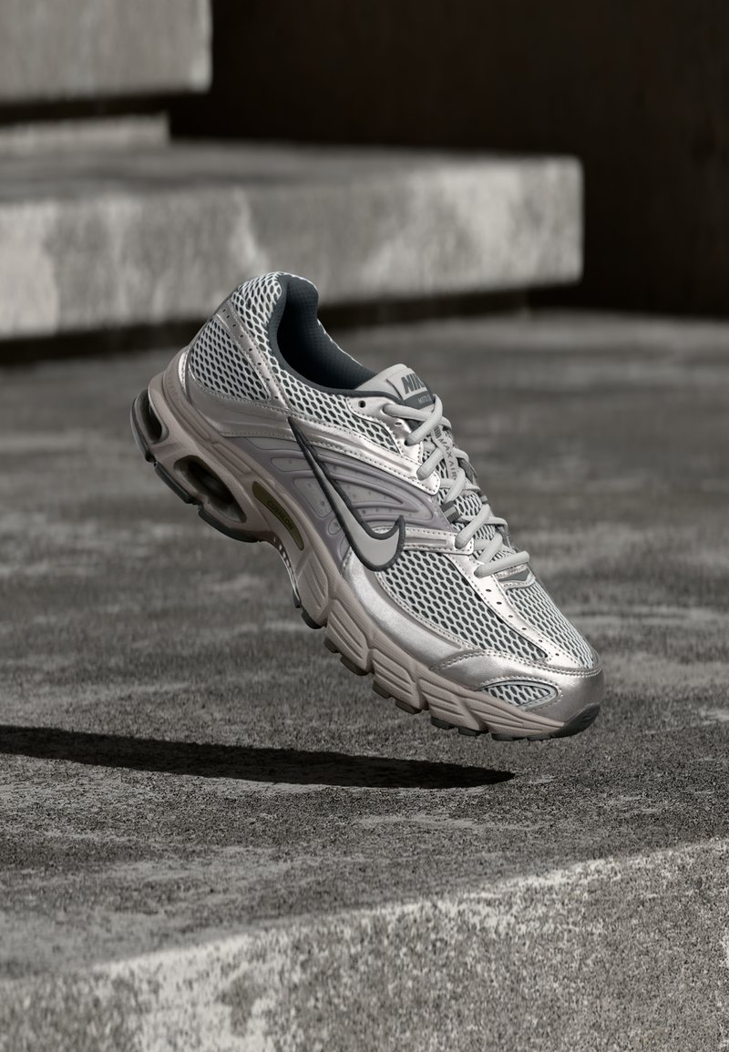 Ασημί και γκρι παπούτσι Nike για τρέξιμο, αιωρούμενο στον αέρα πάνω από σκάλες από σκυρόδεμα, εμφανίζοντας την επάνω επιφάνεια από δίχτυ και τις λεπτομέρειες του μαλακού πάτου.