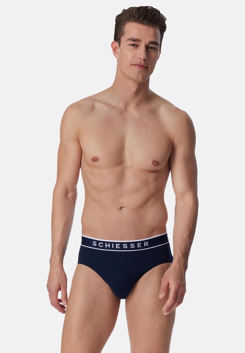 Slip blu navy realizzati in materiale morbido, con una fascia in vita bianca con il logo "SCHIESSER". Design aderente, stile minimalista.