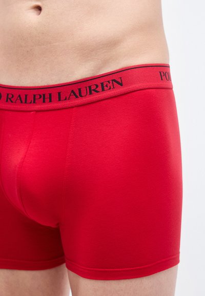 Røde bokserbriefs med svart linning som har "POLO RALPH LAUREN" i fet skrift, laget av glatt, elastisk materiale.