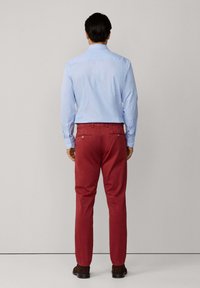 Camisa de botones a rayas azul claro, combinada con pantalones rojos. Los pantalones tienen bolsillos traseros y una textura suave. Unos zapatos marrones oscuros completan el conjunto.