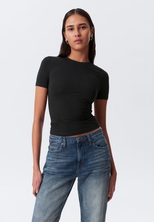 Sort kortærmet tætsiddende t-shirt parret med højtaljede slidte blå jeans, der har et klassisk femlomme-design og knaplukning.