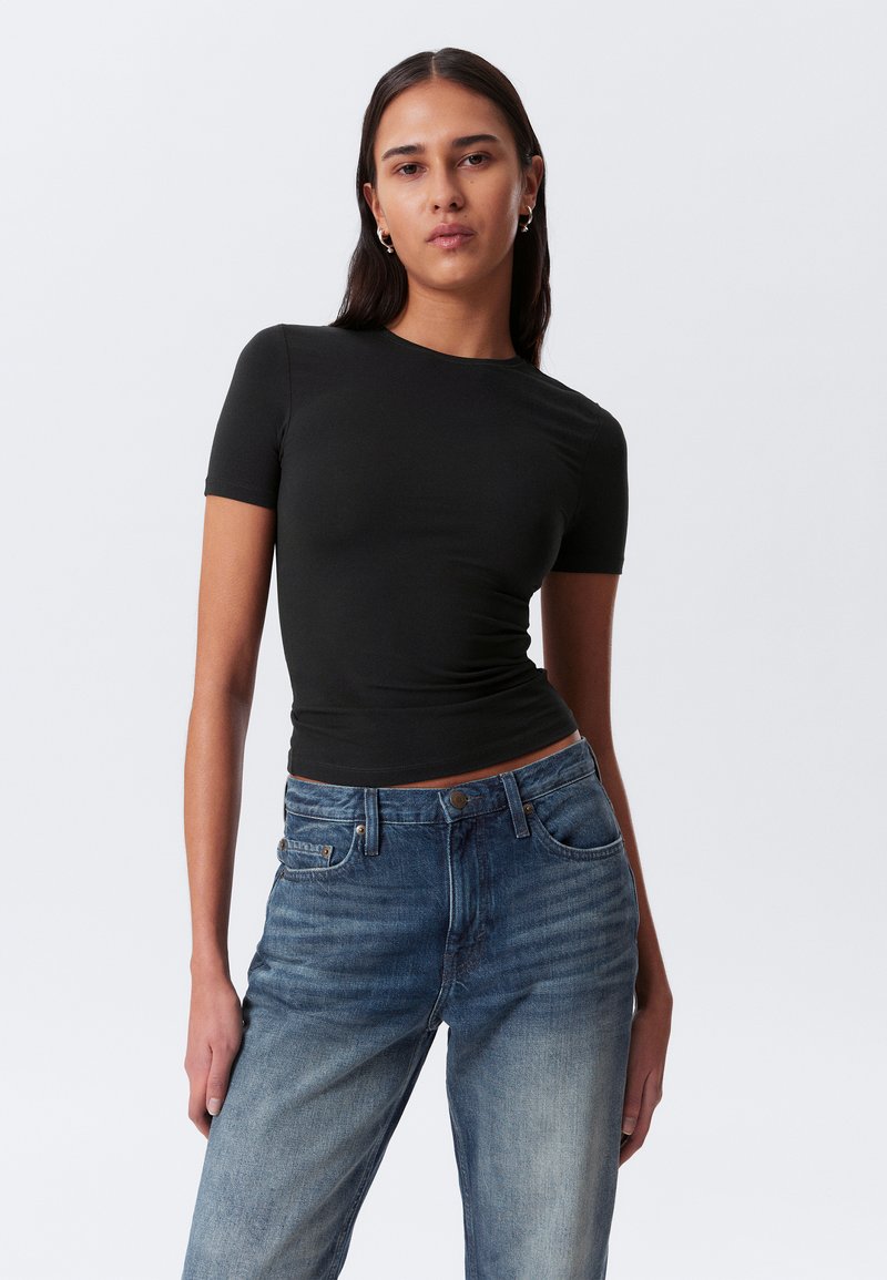 T-shirt noir à manches courtes ajusté associé à un jean bleu déchiré taille haute, doté d'un design classique à cinq poches et d'une fermeture à bouton.