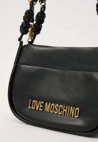 Črna usnjena torbica čez telo s ploskim dizajnom, z vozlanimi črnimi ročaji in logotipom "LOVE MOSCHINO" v zlati barvi.