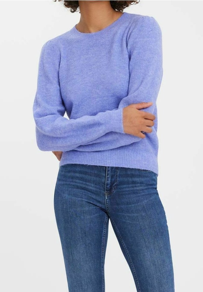 Personne portant un pull douillet lilas à col rond et un jean en denim bleu, bras croisés devant un fond blanc uni.