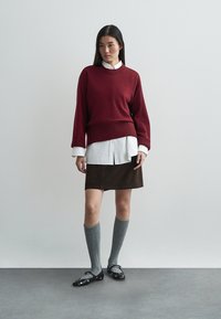 Maroon knit sweater over a white button-up shirt, brown suede skirt, gray knee-high socks, and black flats with white accents.