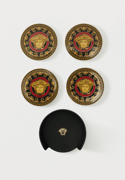 Τέσσερα διακοσμητικά μαύρα και χρυσά πιάτα με σχέδια κεφαλών Μέδουσας πάνω από μια μαύρη στρογγυλή θήκη με χρυσό έμβλημα Μέδουσας σε λευκό φόντο.