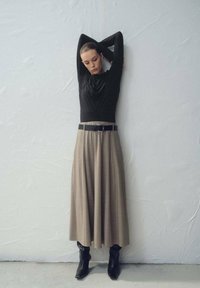 Top negro de manga larga con cuello drapeado, combinado con una falda beige fluida y cinturón negro. Botas negras hasta el tobillo completan el conjunto.