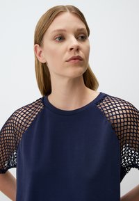 T-shirt blu navy a maniche corte con un design a rete. Il tessuto principale è liscio, in contrasto con i dettagli a rete testurizzati.